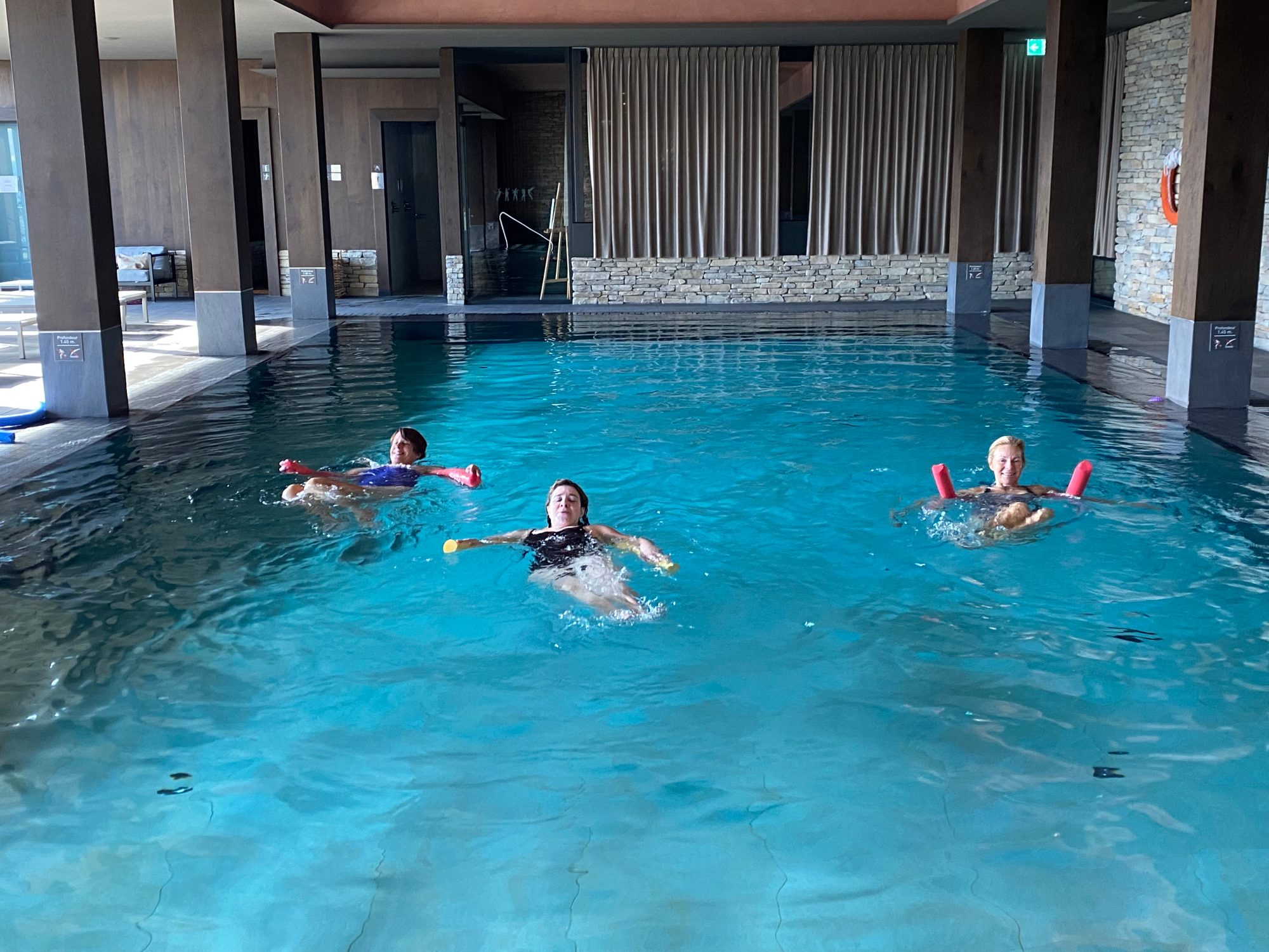 Trois personnes font des exercices dans l’eau d’une piscine, avec des frites de natation