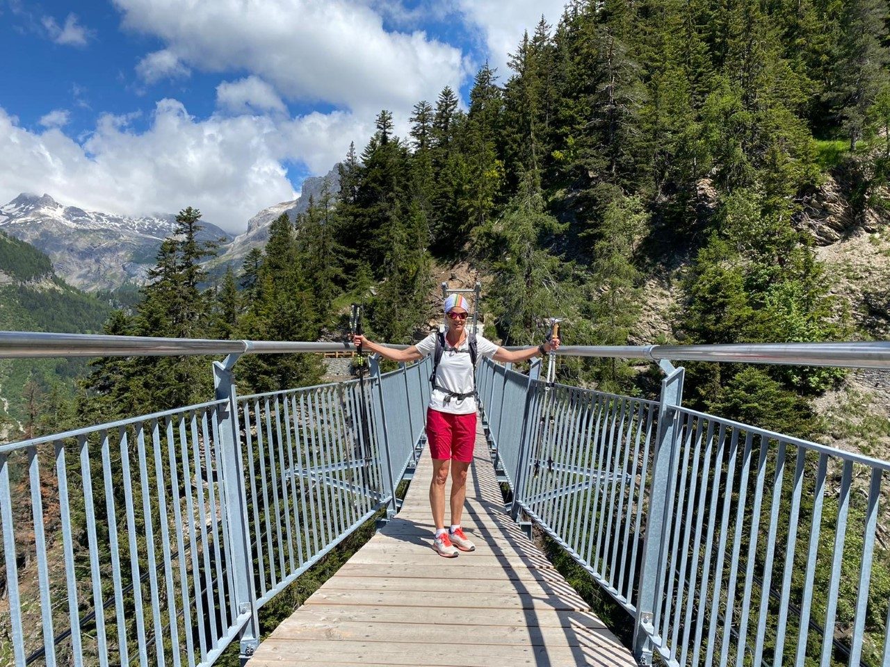 Laetitia Marchand, bâtons de marche en main, bras écartés sur une passerelle suspendue en montagne