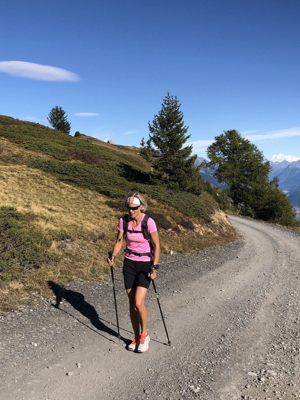 Une femme pratique la marche nordique sur un chemin de gravier, à flanc de colline